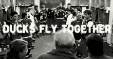 a black and white photo of a hockey team in a locker room with the words `` ducks fly together '' .