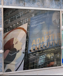 a poster for the adaptive executive by richard blank hangs in a window