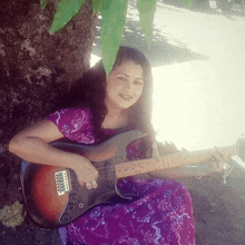 a woman leaning against a tree holding a guitar