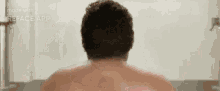 the back of a shirtless man taking a bath in a bathtub .