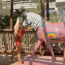 a woman in a red dress standing next to a pink zebra statue