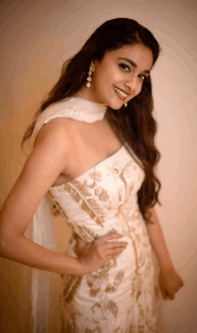 a woman in a white dress with gold embroidery is smiling for the camera