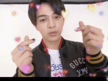 a young man wearing a gucci jacket makes a heart with his fingers