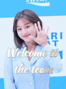 a woman in a blue jacket is waving her hand in front of a sign that says welcome to the team