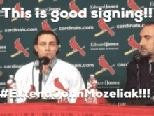 two men sitting at a table with a sign that says " this is good signing " on it