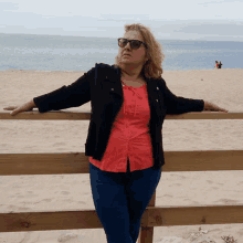 a woman leaning against a wooden fence looking at the ocean