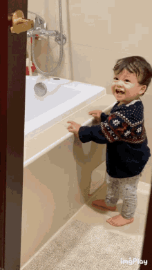 a little boy is standing in front of a bathtub and smiling while wearing a sweater with snowflakes on it