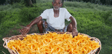 an elderly man sits in the grass holding a basket of french fries