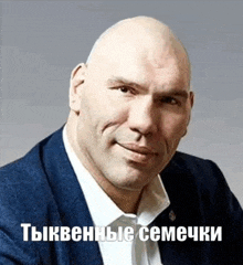 a bald man in a suit and white shirt is smiling with a caption in a foreign language