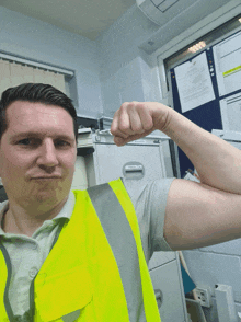 a man wearing a yellow vest flexes his arm