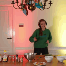 a woman wearing headphones is dancing in front of a table with bowls of food and a bottle of heinz ketchup