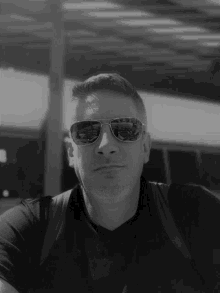 a man wearing sunglasses and a black shirt looks at the camera in a black and white photo