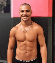 a shirtless man is smiling for the camera while standing in front of a pink wall .