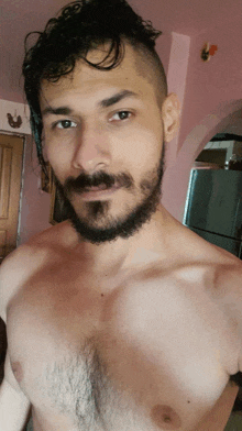 a shirtless man with a beard is taking a selfie in front of a pink wall