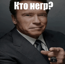 arnold schwarzenegger in a suit and tie pointing with a ring on his finger