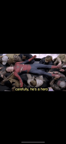 a man in a spiderman costume is laying on the floor surrounded by other people .