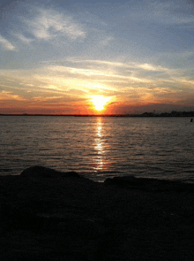 a sunset over a body of water with the sun shining through the clouds