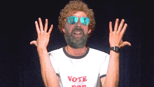 a man with a beard wearing sunglasses and a shirt that says vote for