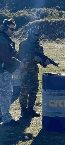 a man in a military uniform is holding a gun next to a barrel that says cycle