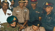 a group of men in military uniforms are standing around a table signing a document .