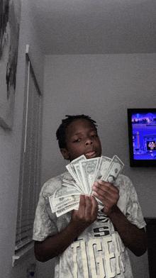 a boy in a tiger t-shirt holds a bunch of money