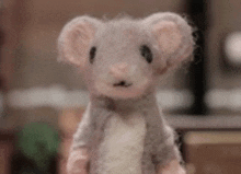 a stuffed mouse is standing in front of a bookshelf and looking at the camera .