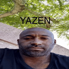 a bald man with a beard stands in front of a tree and the word yazen