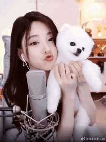 a woman is holding a small white teddy bear in front of a microphone