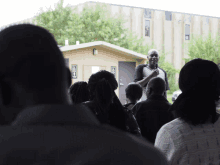 a man stands in front of a group of people in front of a building with a handicapped sign on the door