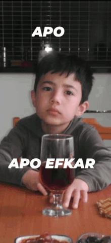 a young boy sits at a table with a glass of red wine and the words apo apo efkar written above him