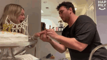 a man is putting a ring on a woman 's finger in front of a cake with a happy birthday banner on top