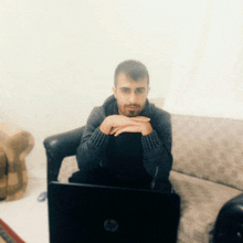 a man sits on a couch with his hands folded in front of a hp laptop