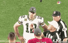 a football player with the number 12 on his jersey is talking to a referee on the field .