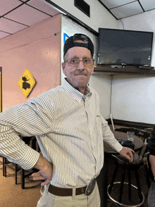 a man wearing a hat and glasses stands with his hands on his hips in a restaurant