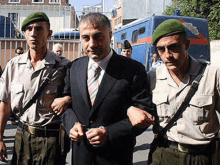 a man in a suit and tie is being escorted by two men in green beret .