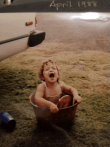 a little girl is sitting in a bucket with the date april 1988 written on the bottom