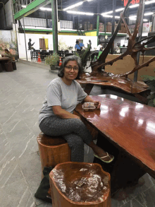 a woman sits at a wooden table with a box of food in her hand