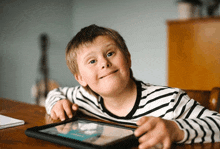 a young boy with down syndrome is sitting at a table with a tablet