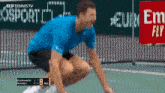 a man in a blue shirt is squatting on a tennis court in front of a sign that says euro fly