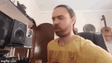 a man with a beard is sitting in a chair in front of a shelf with speakers and guitars .