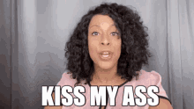 a woman with curly hair is saying kiss my ass in front of a curtain .