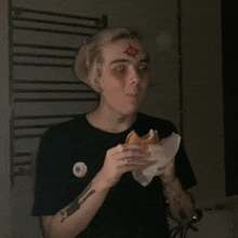 a person with a tattoo on their forehead is eating a sandwich