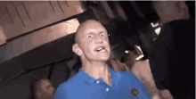 a bald man in a blue shirt is making a funny face in a crowd of people at a party .