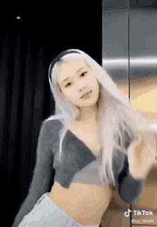 a woman with long white hair is wearing a crop top and shorts and dancing .