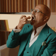 a man wearing a green suit and glasses is eating something