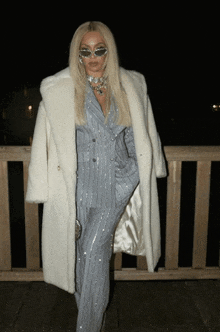 a woman wearing a suit and sunglasses is standing on a railing