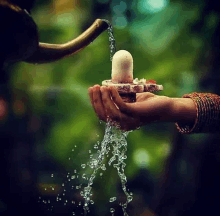 a person is holding a small statue in their hand while water is pouring from a faucet