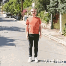 a man in an orange shirt and black jeans is standing on a street in front of a house .