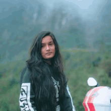 a woman with long hair is standing next to a motorcycle in the woods .