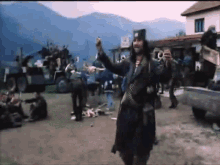 a man in a pirate costume is standing in front of a group of people with mountains in the background .